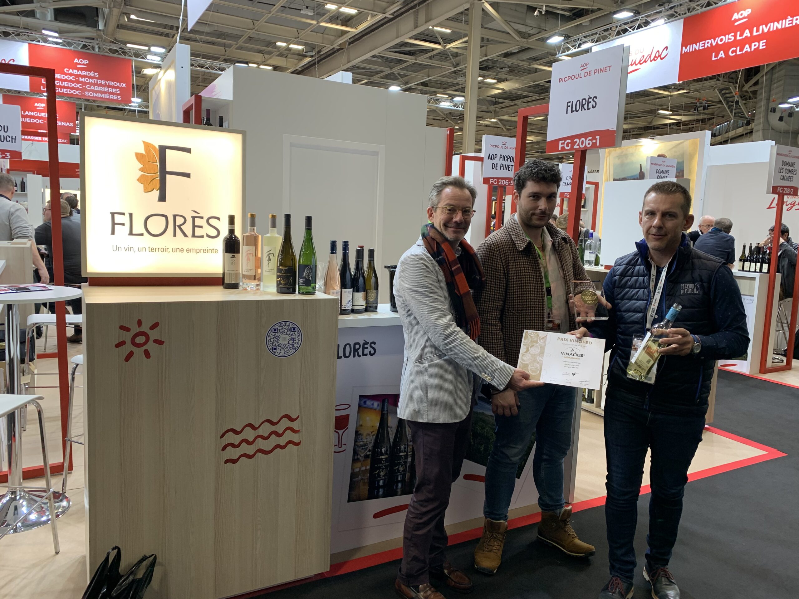 Photographie du stand de Florès où trois responsables Florès présente le Sauvignon Blanc élu Meilleur vin sec du Monde et sa médaille