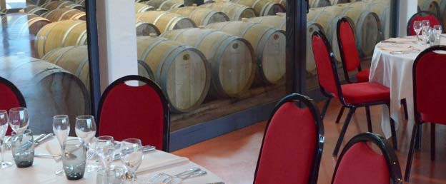 Tables with cutlery and chairs in a reception room overlooking a modern barrel cellar